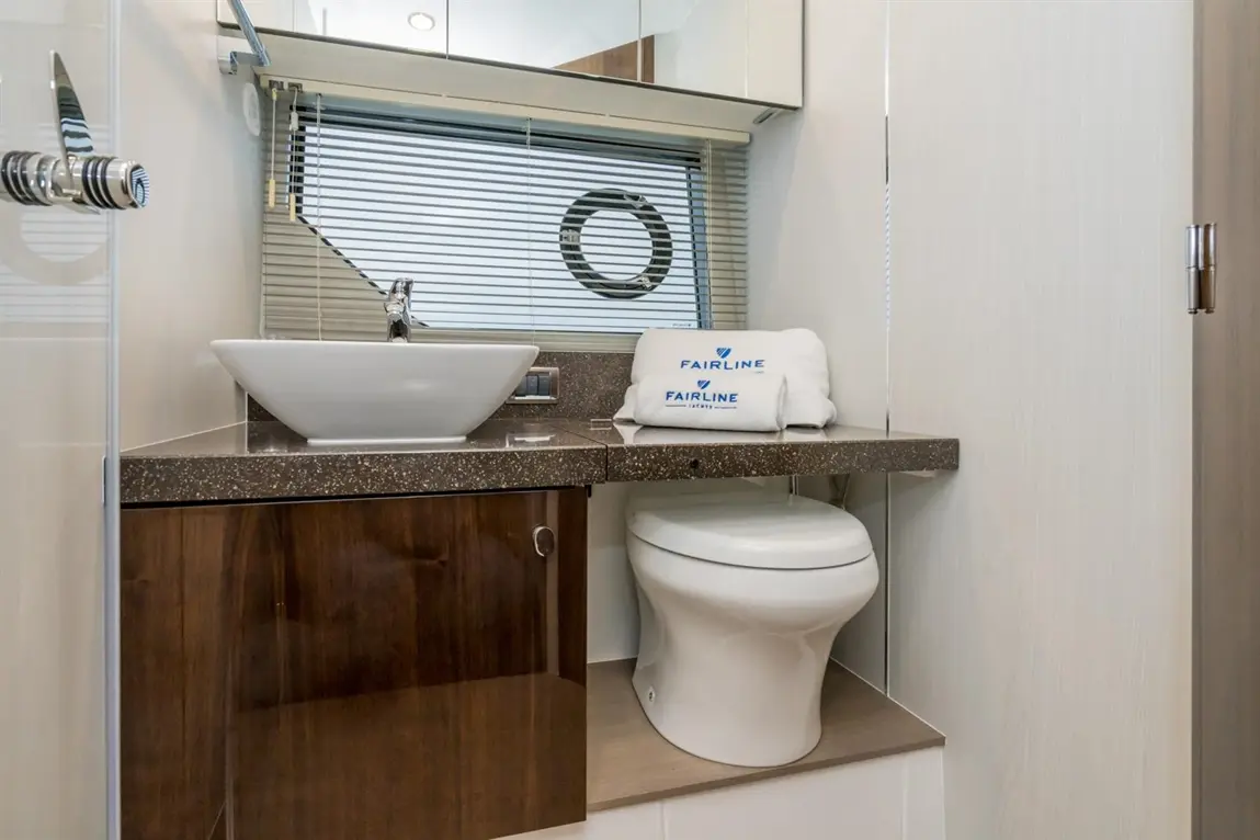 Modern bathroom featuring a round sink, a toilet, a dark countertop, a mirror, and a towel branded "FAIRLINE.